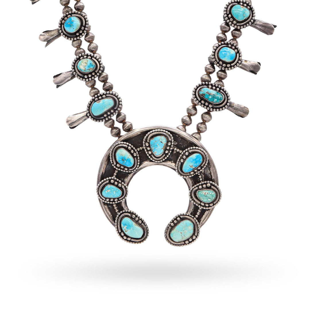 Vintage sterling silver squash blossom necklace with genuine turquoise stones and large naja pendant on a white display bust, showcasing intricate beadwork and traditional Southwest design.