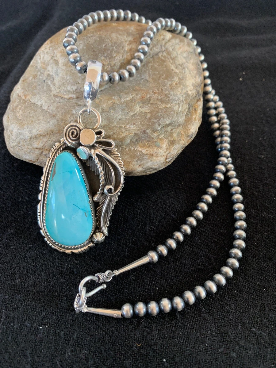 Sterling silver turquoise pendant necklace with large teardrop stone and feather design, displayed on natural stone